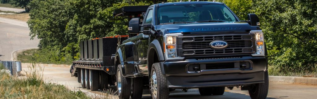 Black Ford Super Duty towing a flatbed trailer on a rural road
