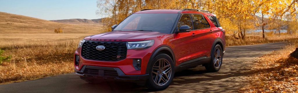 2026 Ford Explorer ST SUV in red, driving through a scenic autumn landscape.