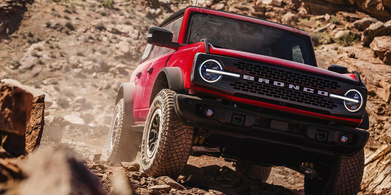 A red Ford Bronco navigating rocky terrain, showcasing its off-road capabilities with large tires and rugged exterior design.