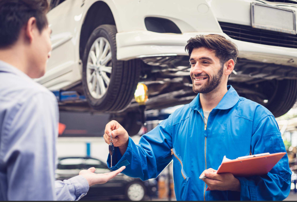 Automotive technician handing car keys to a customer after vehicle service at a repair facility.
