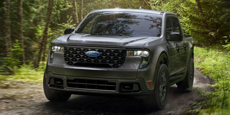  Gray Ford pickup truck driving on a forest trail surrounded by trees.
